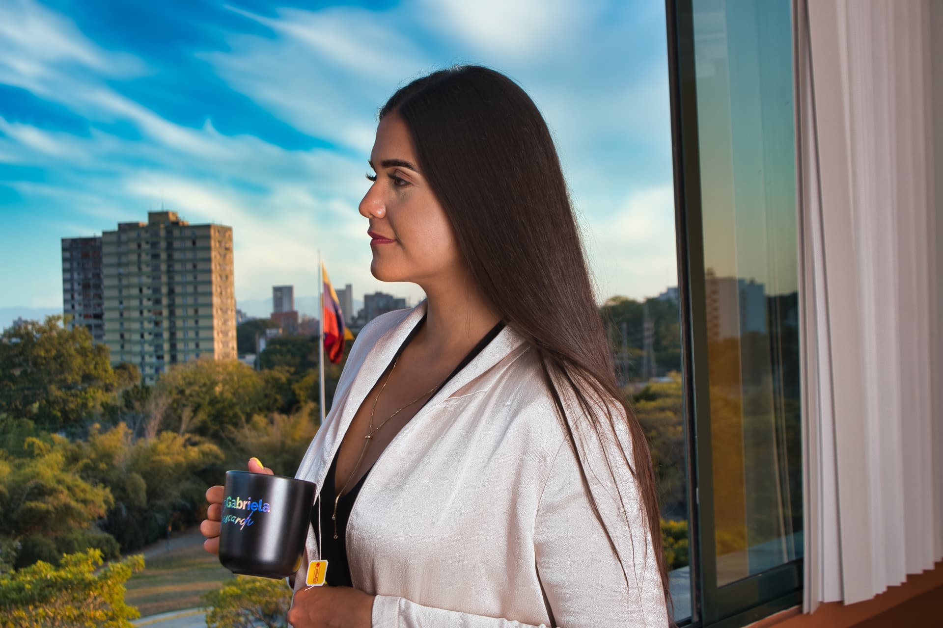 Gabriela by a window in Venezuela, with the Venezuelan flag in the distance